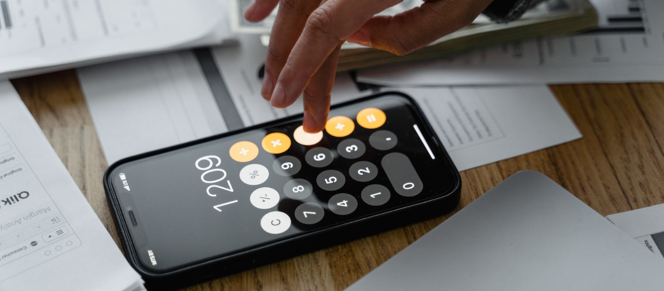 Fingers tapping phone calculator surrounded by papers and money